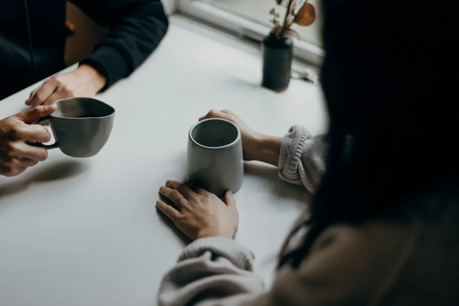 Deux personnes discutent de part et d'autre d'une table, autour d'un café.