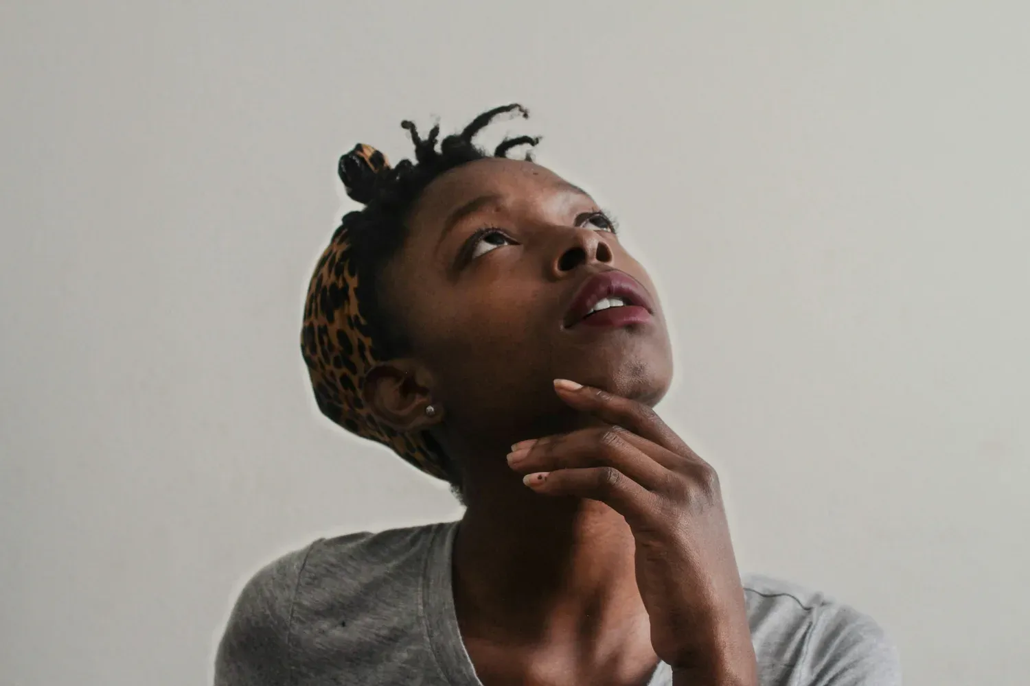 Une femme, la main sous le menton, lève les yeux, pensive.